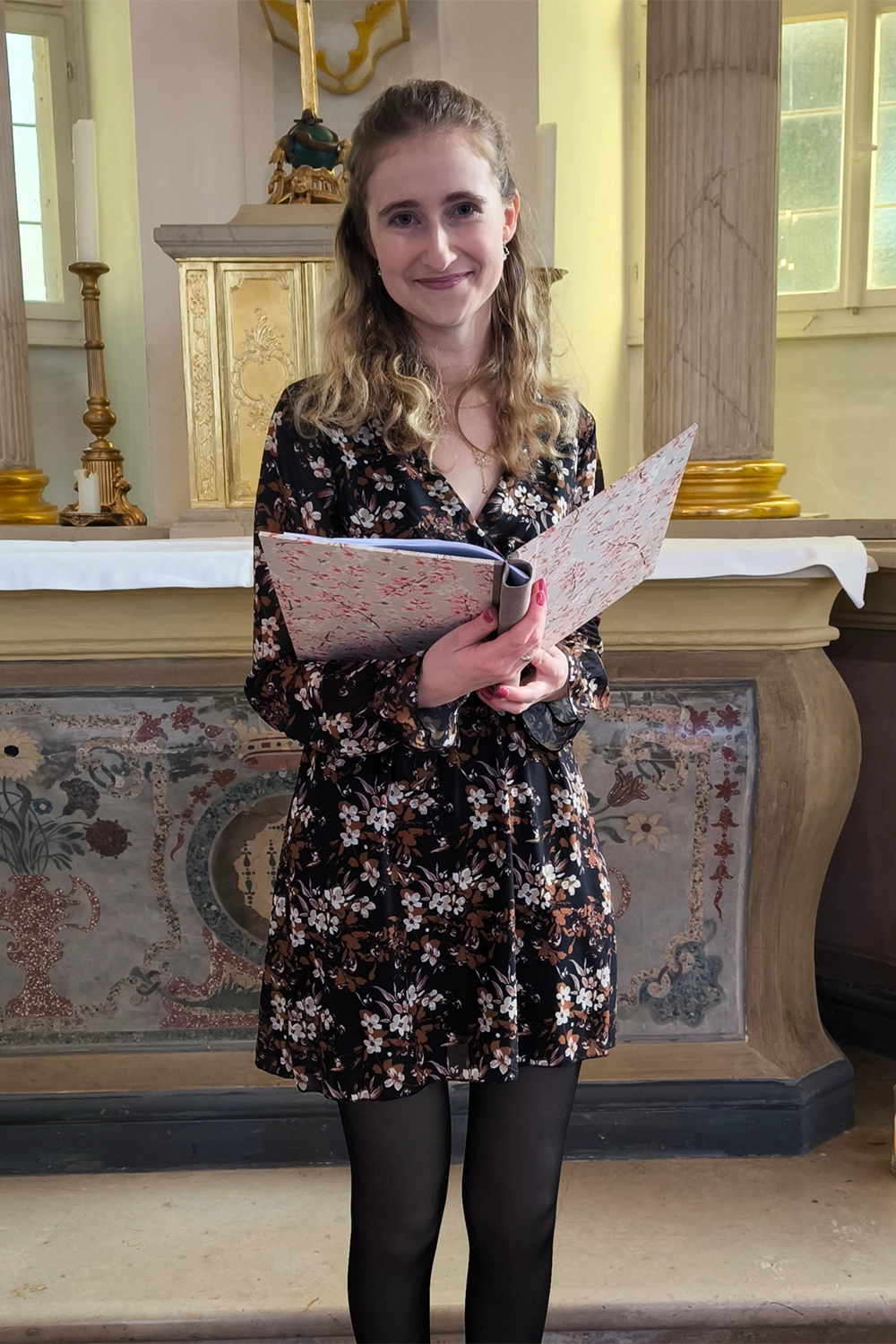 Jasmin Bechstein steht mit ihrem Buch vor einem Altar.